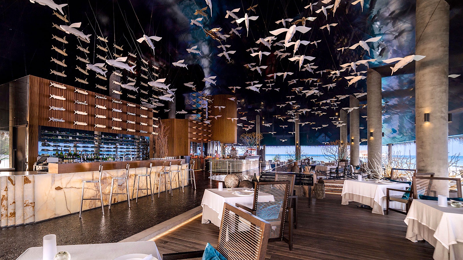The dining room at Aragu with large columns and hanging sculptures of birds and fish